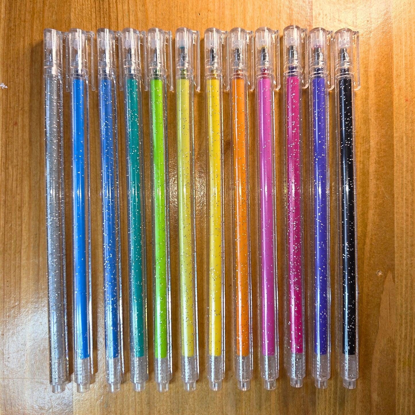 Row of colorful pens with glittery caps on a wooden surface