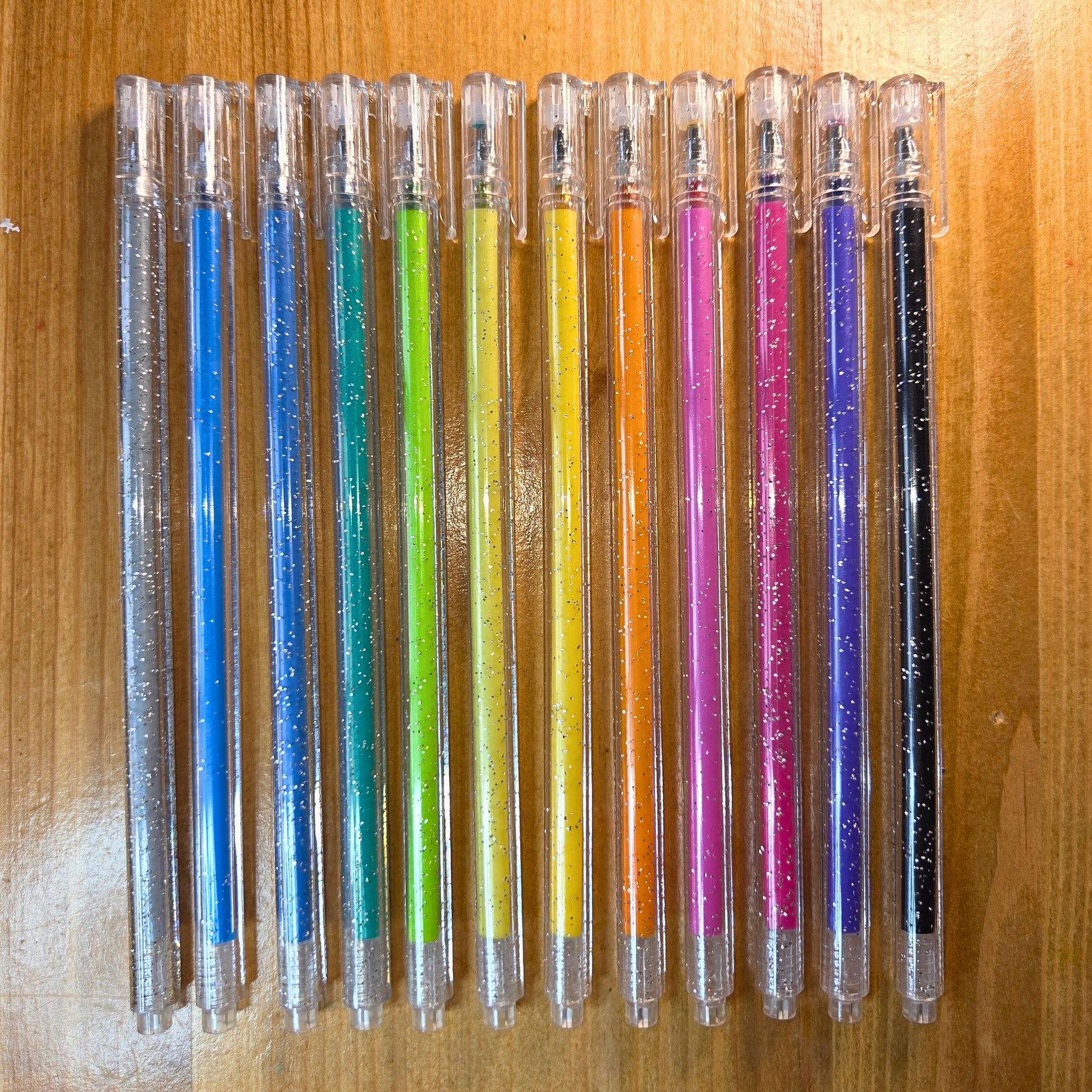 Row of colorful pens with glittery caps on a wooden surface