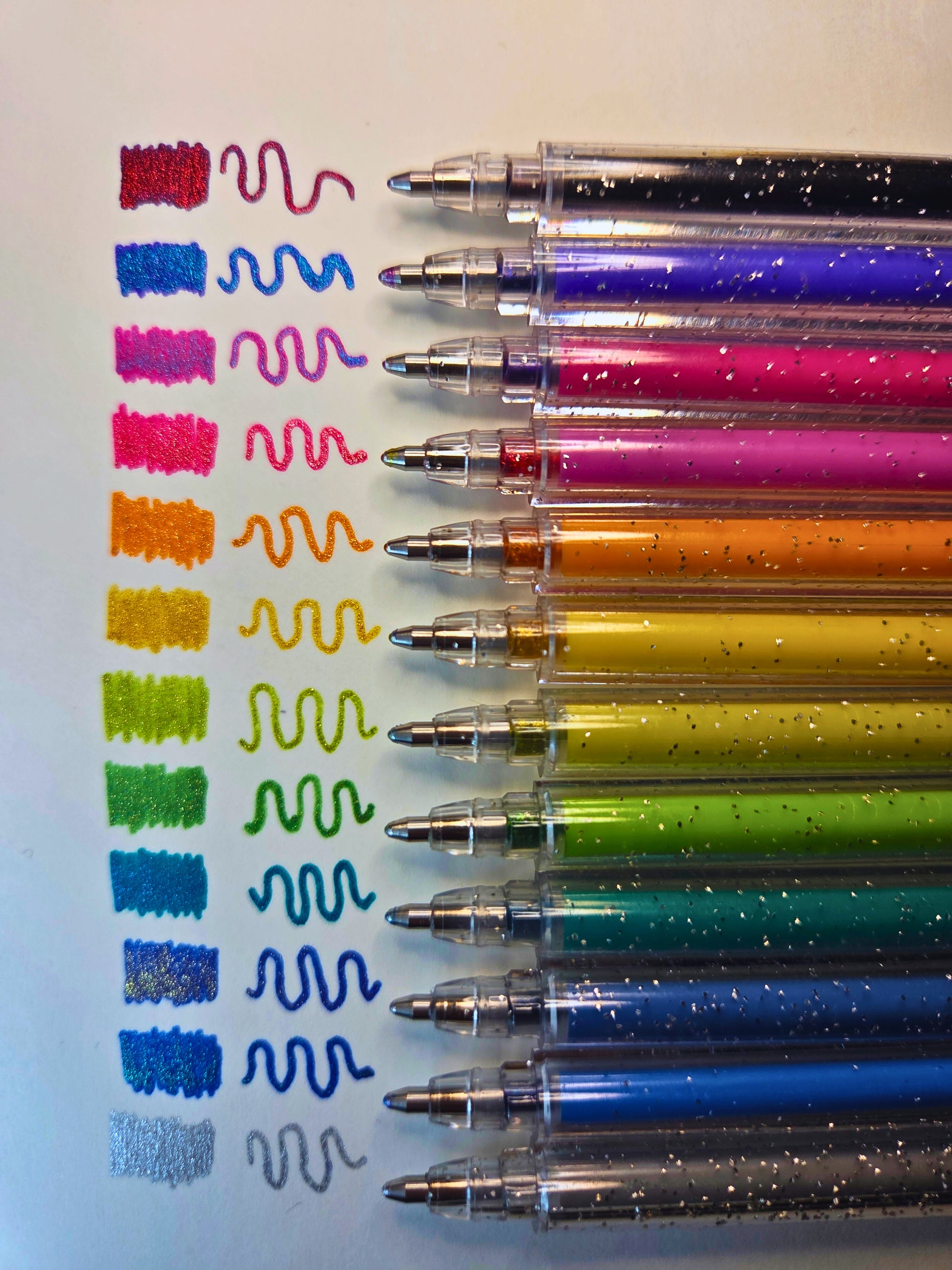 Set of colourful glittery pens with sample lines on a white background