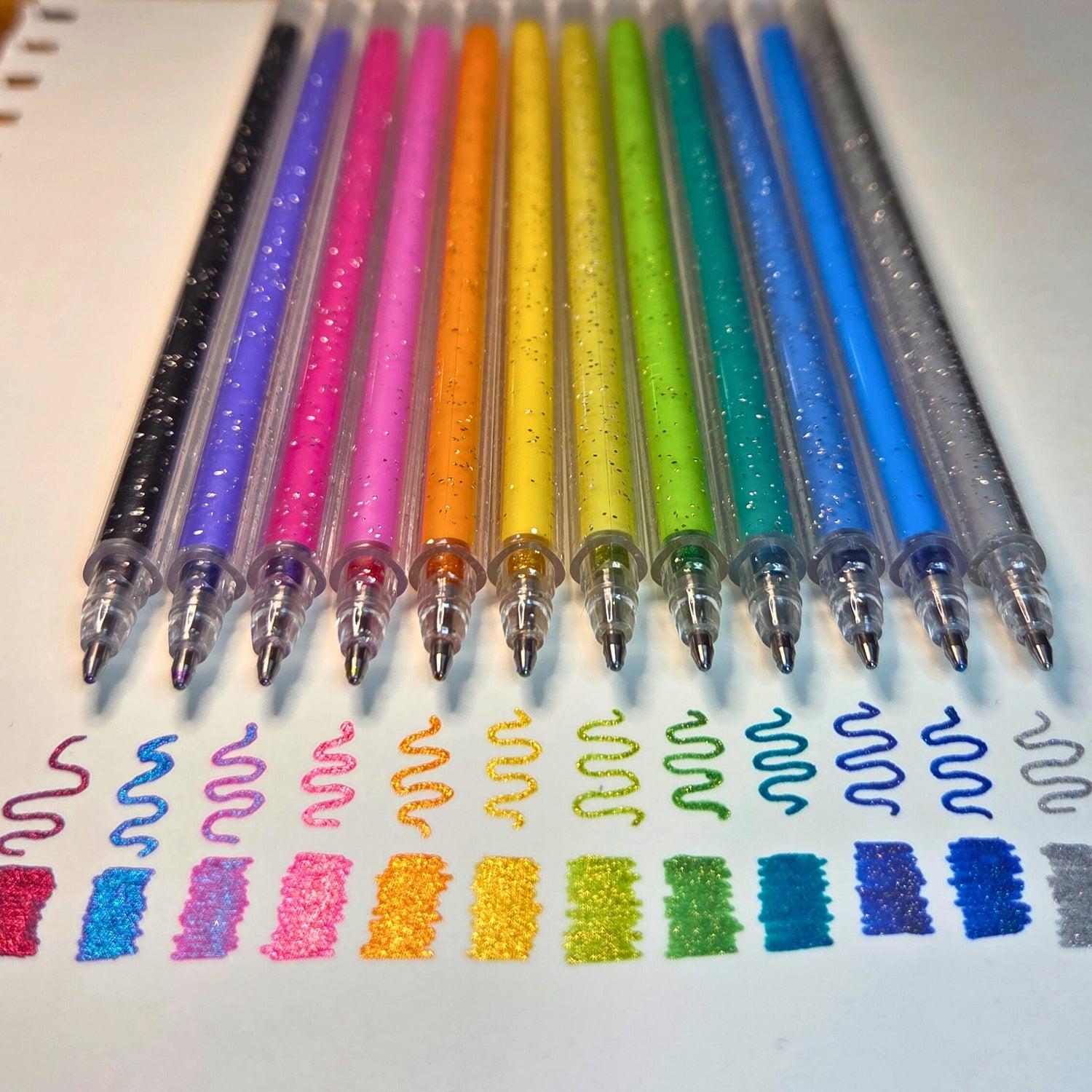 Set of colourful Gemstone Gel pens with sample writing on a white background