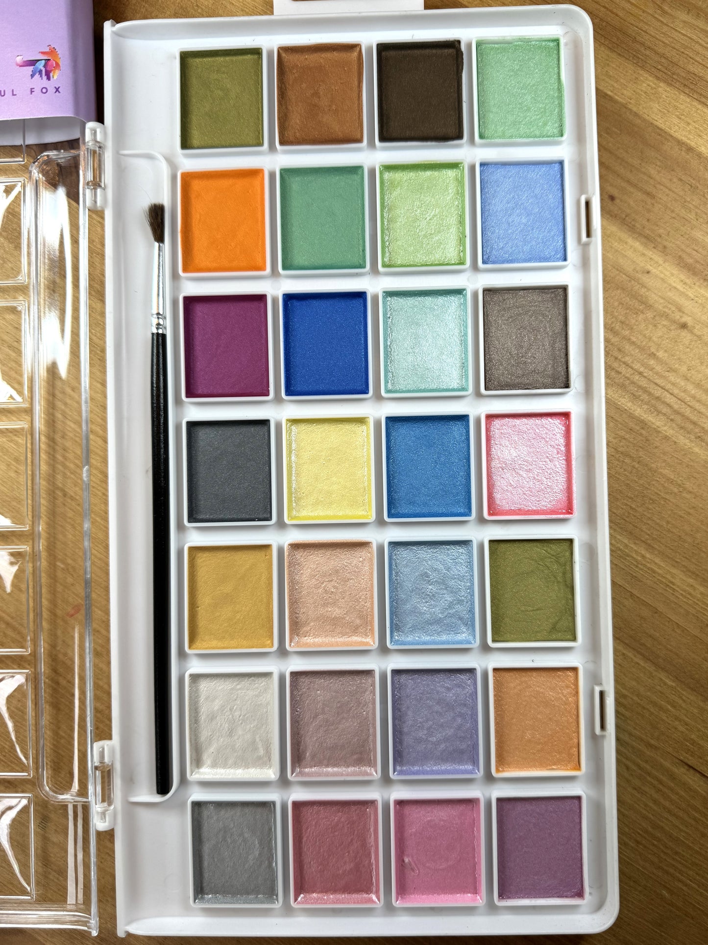 High Shimmer Watercolours by The Artful Fox. 28 pearlescent pastel paints for hobbyists and children, perfect for adding some sparkle to your artwork. Paintbrush included. Storage case with palette lid for mixing your perfect shimmering shade