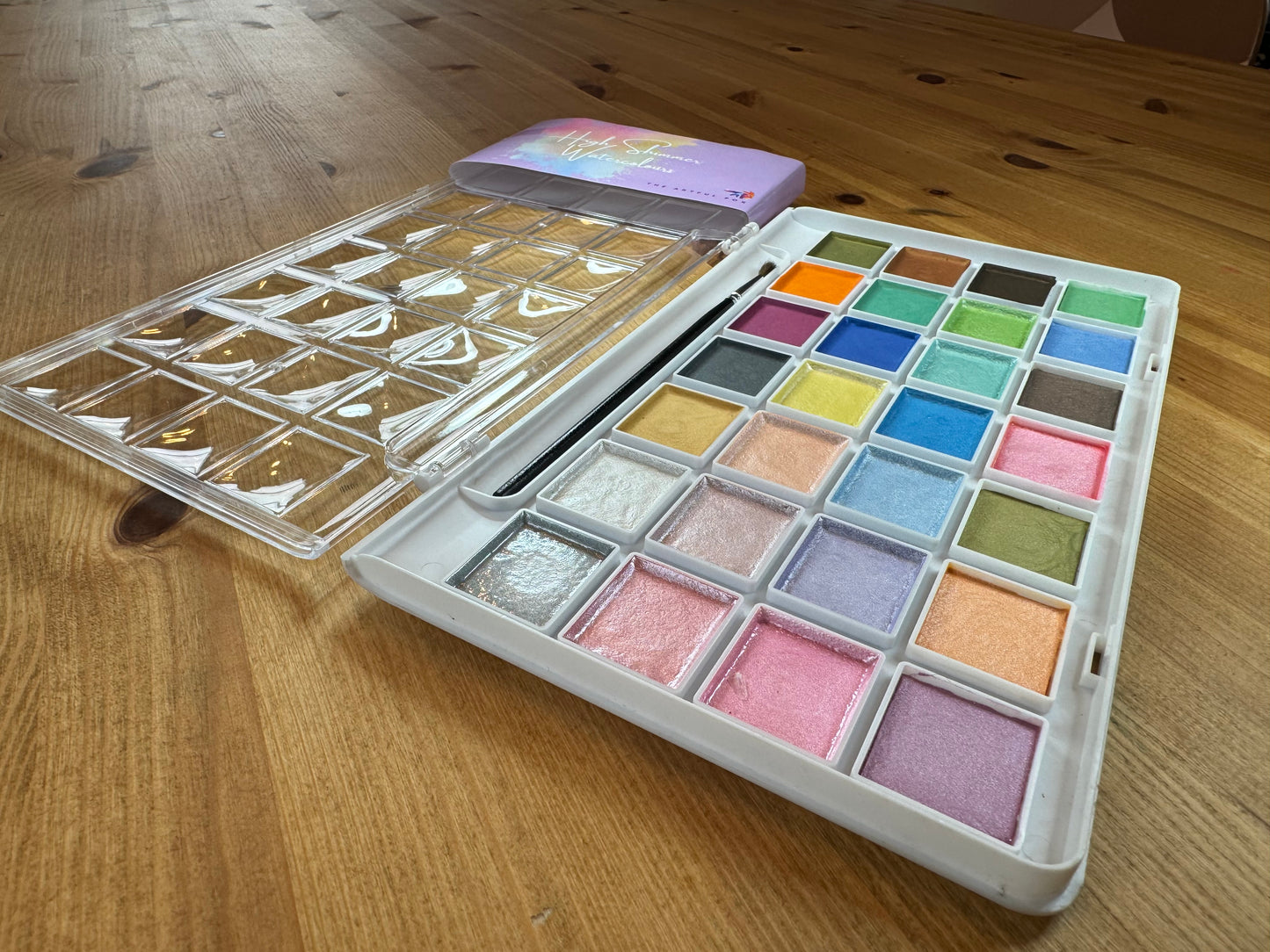 High Shimmer Watercolours by The Artful Fox. 28 pearlescent pastel paints for hobbyists and children, perfect for adding some sparkle to your artwork. Paintbrush included. Storage case with palette lid for mixing your perfect shimmering shade